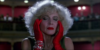 Movie still from “High Heels” (1991), directed by Pedro Almodóvar – An older woman wearing red gloves with her hands up to her face; Close Up shot, Low angle