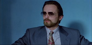 Movie still from “High Heels” (1991), directed by Pedro Almodóvar – A person wearing a suit and sunglasses; Close Up shot, Low angle
