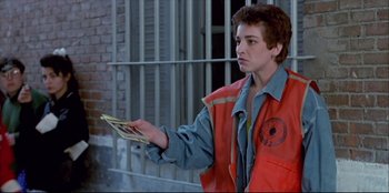 Movie still from “High Heels” (1991), directed by Pedro Almodóvar – A man in an orange vest holding a bunch of money; Medium shot, Low angle