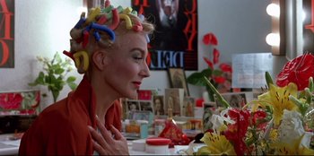 Movie still from “High Heels” (1991), directed by Pedro Almodóvar – A woman sitting in front of a table with flowers in her hair; Close Up shot, Over the shoulder angle