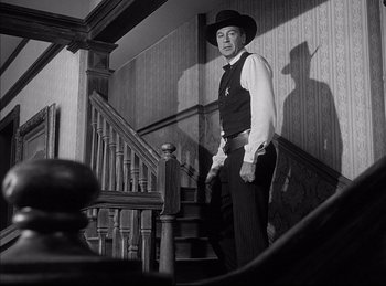 Movie still from “High Noon” (1952), directed by Fred Zinnemann – A black and white photo of a man standing on the stairs; Medium shot, Low angle