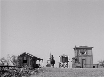 Movie still from “High Noon” (1952), directed by Fred Zinnemann – A man riding a horse in a dirt field next to buildings; Extreme Wide shot, Low angle