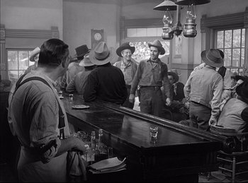 Movie still from “High Noon” (1952), directed by Fred Zinnemann – A black and white photo of a group of men standing around a bar; Wide shot, Over the shoulder angle