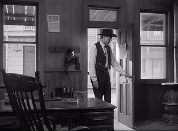 Movie still from “High Noon” (1952), directed by Fred Zinnemann – A black and white photo of a man opening a door; Wide shot, Low angle