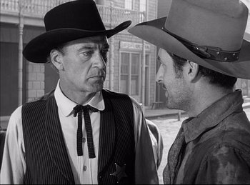 Movie still from “High Noon” (1952), directed by Fred Zinnemann – A man in a cowboy hat talking to another man in a cowboy hat; Medium shot, Over the shoulder angle