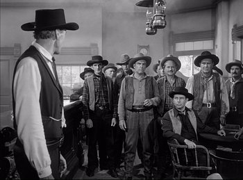 Movie still from “High Noon” (1952), directed by Fred Zinnemann – A black and white photo of a group of men in hats; Medium shot, Over the shoulder angle