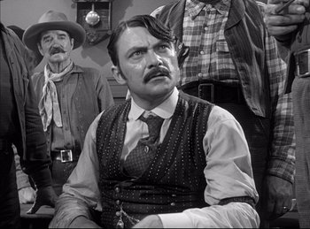 Movie still from “High Noon” (1952), directed by Fred Zinnemann – A black and white photo of a man with a mustache; Medium shot, Over the shoulder angle