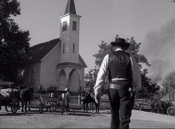 Movie still from “High Noon” (1952), directed by Fred Zinnemann – A man in a cowboy hat is standing in front of a church; Wide shot, Low angle