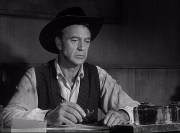 Movie still from “High Noon” (1952), directed by Fred Zinnemann – An old photo of a man sitting at a table writing; Medium shot, Low angle