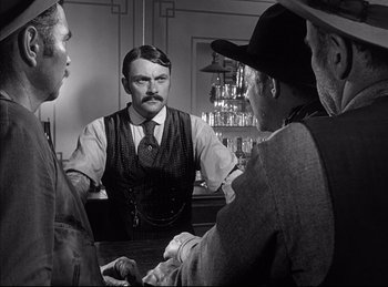 Movie still from “High Noon” (1952), directed by Fred Zinnemann – A man with a mustache sitting at a bar with two other men; Medium shot, Over the shoulder angle