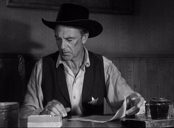 Movie still from “High Noon” (1952), directed by Fred Zinnemann – A man in a cowboy hat writing on a piece of paper at a table; Medium shot, Low angle
