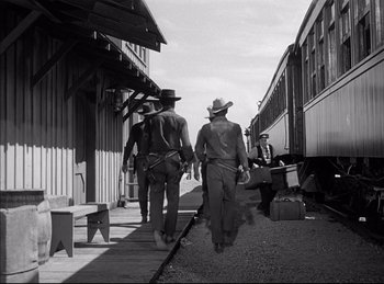 Movie still from “High Noon” (1952), directed by Fred Zinnemann – A black - and - white photo of men walking down a train platform; Wide shot, Low angle