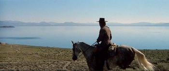 Movie still from “High Plains Drifter” (1973), directed by Clint Eastwood – A man riding on the back of a white horse; Wide shot, Low angle