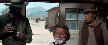 Movie still from “High Plains Drifter” (1973), directed by Clint Eastwood – A man is shaving his face in front of a building; Medium shot, Over the shoulder angle