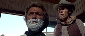 Movie still from “High Plains Drifter” (1973), directed by Clint Eastwood – A man with a beard and a hat is shaving his face; Close Up shot, Low angle
