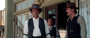 Movie still from “High Plains Drifter” (1973), directed by Clint Eastwood – A man in a hat standing next to another man in a suit; Medium shot, Low angle