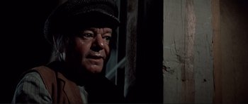 Movie still from “High Plains Drifter” (1973), directed by Clint Eastwood – An older man wearing a hat standing next to a wall; Close Up shot, Over the shoulder angle