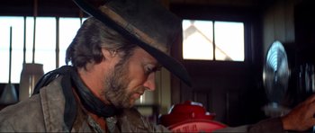 Movie still from “High Plains Drifter” (1973), directed by Clint Eastwood – A man with a cowboy hat on looking down at a fire hydrant; Close Up shot, Low angle