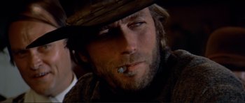 Movie still from “High Plains Drifter” (1973), directed by Clint Eastwood – A person wearing a hat and smoking a cigarette; Close Up shot, Low angle