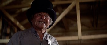 Movie still from “High Plains Drifter” (1973), directed by Clint Eastwood – An older man wearing a black hat in a room; Close Up shot, Low angle