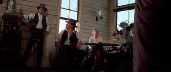 Movie still from “High Plains Drifter” (1973), directed by Clint Eastwood – A group of people sitting around a table; Wide shot, Low angle