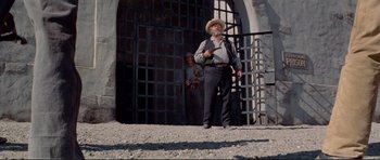 Movie still from “High Plains Drifter” (1973), directed by Clint Eastwood – An old man standing in front of an iron gate; Wide shot, Low angle