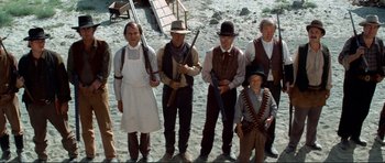 Movie still from “High Plains Drifter” (1973), directed by Clint Eastwood – A group of people standing next to each other holding guns; Wide shot, Low angle