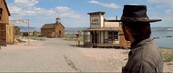 Movie still from “High Plains Drifter” (1973), directed by Clint Eastwood – A man standing on a ladder in front of a building on a dirt road; Extreme Wide shot, Low angle