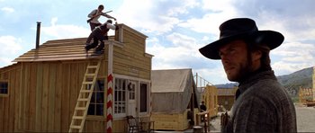 Movie still from “High Plains Drifter” (1973), directed by Clint Eastwood – A man in a cowboy hat is standing on a wooden structure; Wide shot, Low angle
