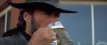Movie still from “High Plains Drifter” (1973), directed by Clint Eastwood – A man in a cowboy hat drinking a glass of beer; Close Up shot, Low angle