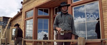 Movie still from “High Plains Drifter” (1973), directed by Clint Eastwood – A man in a cowboy hat holding a gun and holding a beer; Medium shot, Low angle