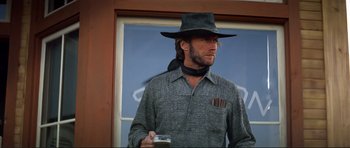 Movie still from “High Plains Drifter” (1973), directed by Clint Eastwood – A man in a cowboy hat holding a beer; Medium shot, Low angle