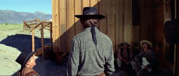 Movie still from “High Plains Drifter” (1973), directed by Clint Eastwood – A man wearing a cowboy hat standing in front of a wooden wall; Medium shot, Over the shoulder angle