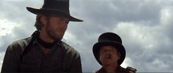 Movie still from “High Plains Drifter” (1973), directed by Clint Eastwood – A man and a man with a hat on; Close Up shot, Low angle