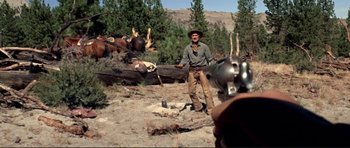 Movie still from “High Plains Drifter” (1973), directed by Clint Eastwood – A man holding a gun while standing on a dirt field; Wide shot, Over the shoulder angle