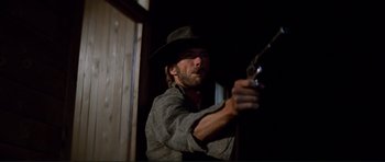 Movie still from “High Plains Drifter” (1973), directed by Clint Eastwood – A man holding a gun in a dark room; Close Up shot, Low angle