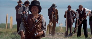 Movie still from “High Plains Drifter” (1973), directed by Clint Eastwood – A group of people standing on top of a grass covered hill; Medium shot, Low angle