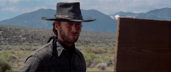 Movie still from “High Plains Drifter” (1973), directed by Clint Eastwood – A man in a hat and a jacket standing in a field; Close Up shot, Low angle