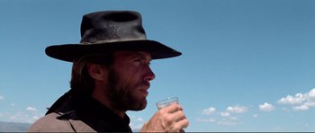 Movie still from “High Plains Drifter” (1973), directed by Clint Eastwood – A man in a hat holding a glass in his hand; Close Up shot, Low angle