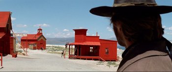 Movie still from “High Plains Drifter” (1973), directed by Clint Eastwood – A man in a cowboy hat standing in front of a red building; Extreme Wide shot, Low angle