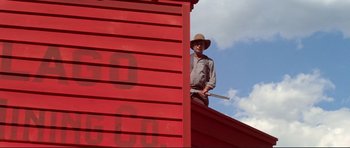 Movie still from “High Plains Drifter” (1973), directed by Clint Eastwood – A man standing on the side of a red building; Wide shot, Low angle
