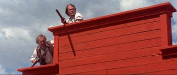 Movie still from “High Plains Drifter” (1973), directed by Clint Eastwood – A man standing on top of a red building; Medium shot, Low angle