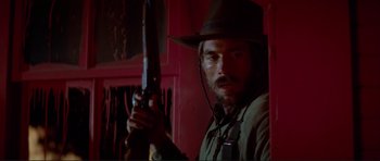Movie still from “High Plains Drifter” (1973), directed by Clint Eastwood – A man holding a rifle in a room; Close Up shot, Low angle