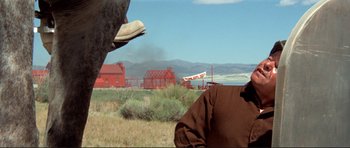 Movie still from “High Plains Drifter” (1973), directed by Clint Eastwood – A man standing in a field near a red building; Medium shot, Low angle