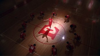 Movie still from “High School Musical” (2006), directed by Kenny Ortega – A group of young men sitting on top of a basketball court; Extreme Wide shot, Overhead angle