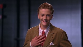 Movie still from “High School Musical” (2006), directed by Kenny Ortega – A young man in a suit and a red tie smiling; Close Up shot, High angle