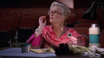 Movie still from “High School Musical” (2006), directed by Kenny Ortega – An older woman sitting at a table with a cell phone in front of her face; Medium shot, Low angle