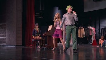 Movie still from “High School Musical” (2006), directed by Kenny Ortega – A man and a woman are on stage singing; Wide shot, Low angle
