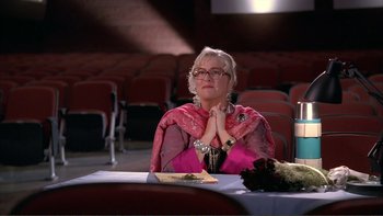 Movie still from “High School Musical” (2006), directed by Kenny Ortega – An older woman sitting at a table in front of an audience; Medium shot, High angle