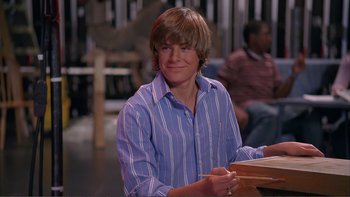 Movie still from “High School Musical” (2006), directed by Kenny Ortega – A man sitting at a table with a book in his hands; Medium shot, Low angle